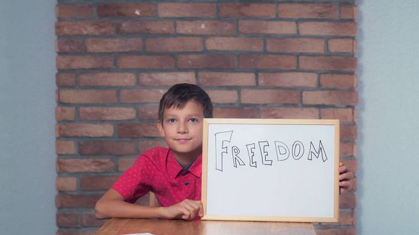 ребенок сидит за столом держа флипчарт с надписью освобожден
 - Фото, изображение