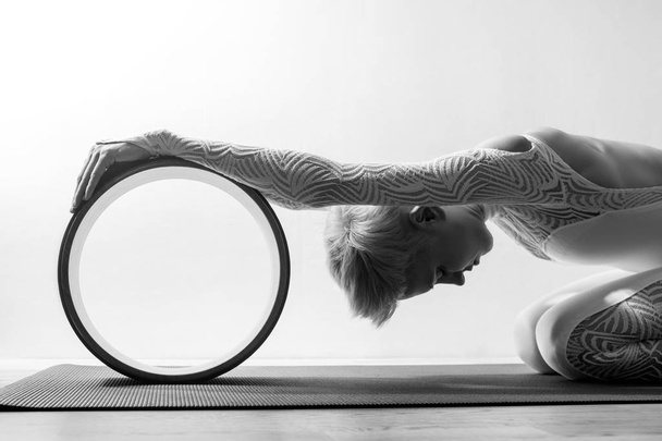 Portrait of gorgeous young woman practicing yoga indoor with a help of yoga wheel - Valokuva, kuva