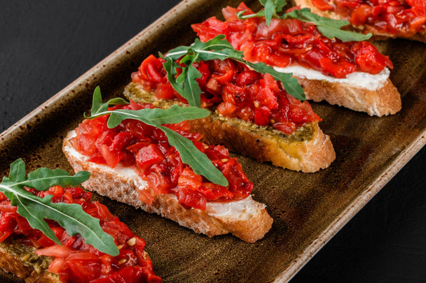 Appetizer bruschetta with chopped vegetables on ciabatta bread and sauce pesto on plate over black stone background. Vegetarian food concept. Delicious snacks, crostini, canape on picnic time - Photo, Image
