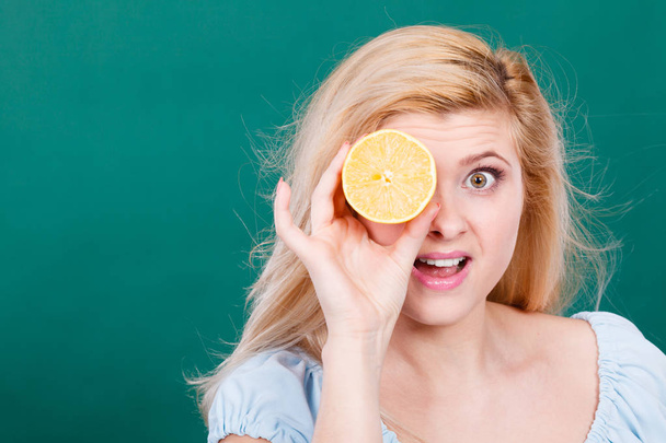 Woman teen girl holding half of yellow lemon citrus fruit in hand, covering her eye, on dark green. Healthy diet nutrition. Happiness fun concept. - Фото, зображення