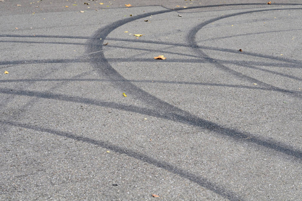 καμπυλωτή μαύρη αντιολισθητικές σήματα σε ασφαλτοστρωμένο δρόμο με ξηρό σφενδάμου φύλλα - Φωτογραφία, εικόνα