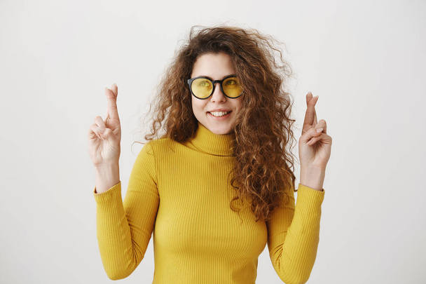 Возбужденная женщина в желтом свитере держит пальцы скрещенными, рот широко открыт, ожидая особого момента изолированы на сером фоне
. - Фото, изображение