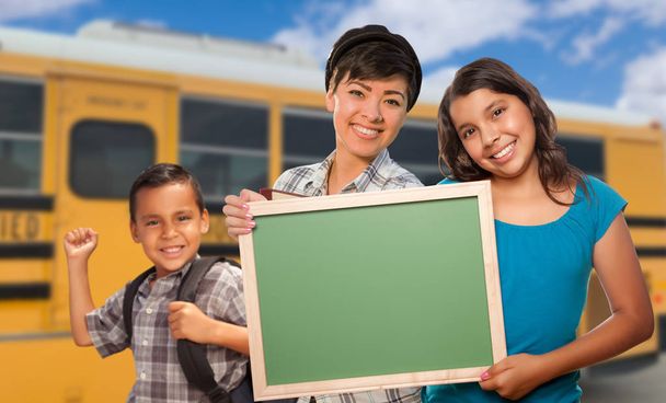 Jong gemengd ras studenten met leeg schoolbord in de buurt van schoolbus. - Foto, afbeelding