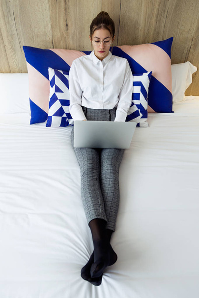 Shot of beautiful young businesswoman working with her laptop lying on bed in the hotel room. - Фото, зображення
