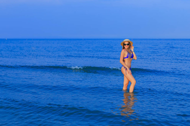 chica en un traje de baño azul, gafas de sol y boater posa en agua de mar
 - Foto, imagen