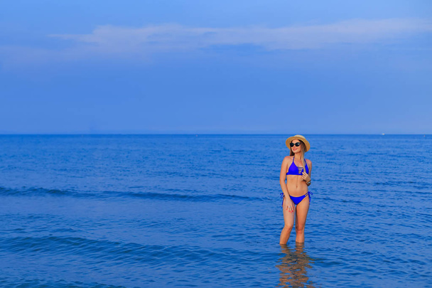  Chica joven en un traje de baño azul y gafas de sol está posando en agua de mar
 - Foto, imagen