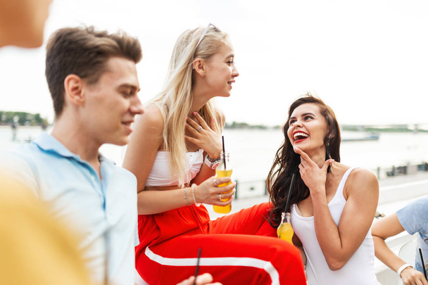 Une compagnie de beaux amis riant et buvant des cocktails jaunes et socialisant dans le joli café à côté de la rivière. À la tienne. Divertissement, s'amuser. River est en arrière-plan
. - Photo, image