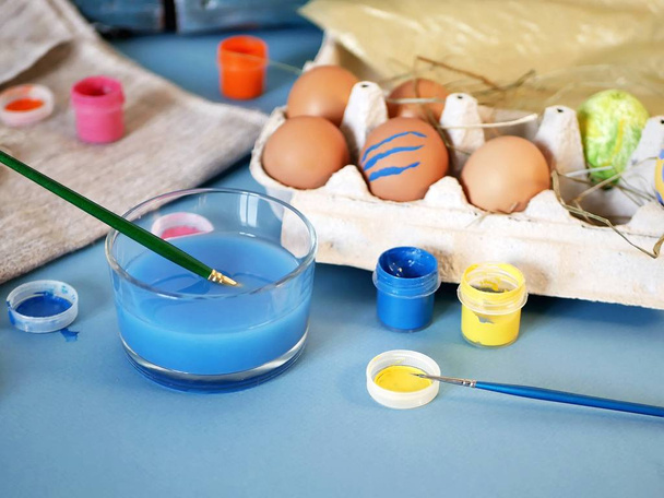 Eggs, colorful paints, brushes, pencils on a blue background, coloring eggs, preparing for Easter, spring seasonal holiday - Zdjęcie, obraz