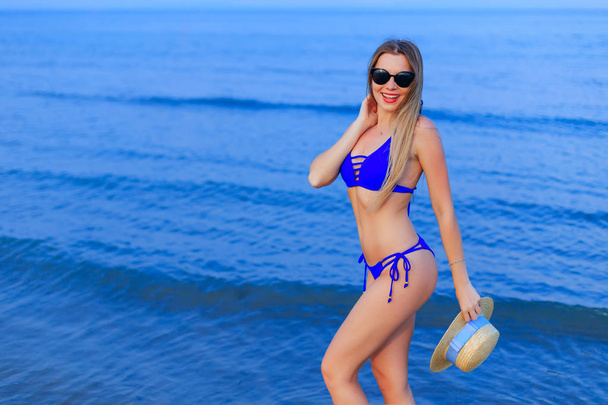 Pretty girl with sunglasses in blue swimsuit poses on the background of the sea - Photo, Image