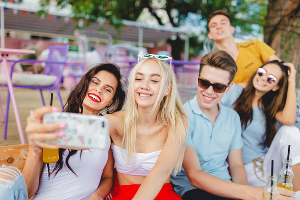 Een gezelschap van knappe vrienden lachen en drinken gele cocktails, gezelligheid en het maken van de selfie aan de tafel in het mooie zomerterras. Cheers. Entertainment, met goede tijd. Vriendschap. - Foto, afbeelding