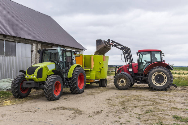 El tractor con cargador frontal carga la comida en un distribuidor de alimento para animales para vacas. Equipo necesario para una granja lechera
. - Foto, imagen