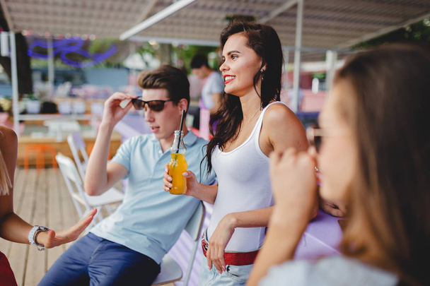A company of good-looking friends laughing, drinking yellow cocktails and socialising at the bar in the nice summer cafe. Cheers. Entertainment, having good time. Friendship. - 写真・画像