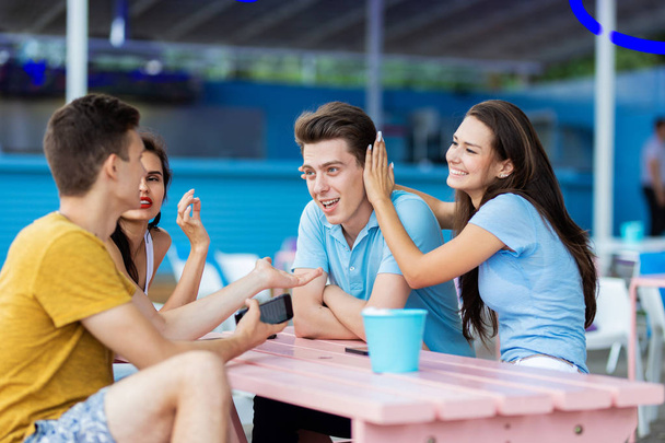 A company of good-looking friends is laughing and sitting at the table in the nice summer cafe. Entertainment, having good time. Friendship. - Фото, зображення