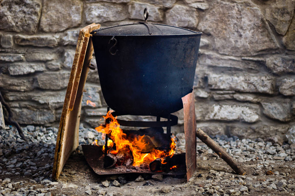 Cocinero tradicional en un caldero de hierro fundido. Comida en una llama abierta. Sartén para cocinar para muchas personas
 - Foto, Imagen