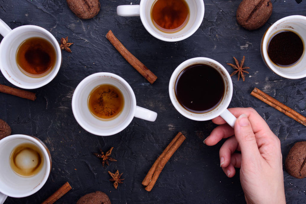 Delicious and fragrant coffee in the form of coffee, with grains of coffee. Cups of coffee in beautiful cups. Cinnamon sticks on a black background - Photo, Image