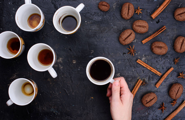 Heerlijke en geurige koffie in de vorm van koffie, met korrels van koffie. Kopjes koffie in mooie bekers. Kaneelstokjes op een zwarte achtergrond - Foto, afbeelding