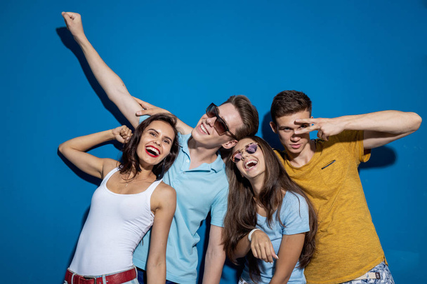 Four good-looking friends are laughing while standing in front of the blue wall having confident and happy looks. Entertainment, having good time. Friendship, relationship. - Fotografie, Obrázek