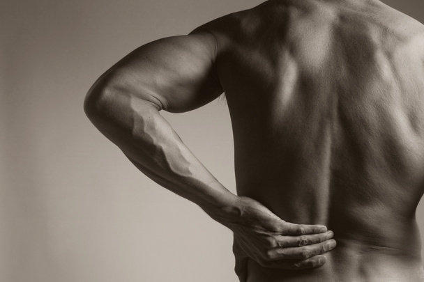 Homem segurando sua parte inferior das costas como se experimentando uma dor nas costas
 - Foto, Imagem