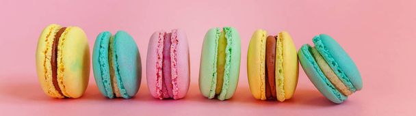 Słodki migdałowy kolorowy jednorożec różowy niebieski żółty zielony makaron lub makaron deser ciasto izolowane na modnym różowym tle pastelowym. Francuskie słodycze. Minimalna koncepcja piekarni żywności. Sztandar - Zdjęcie, obraz