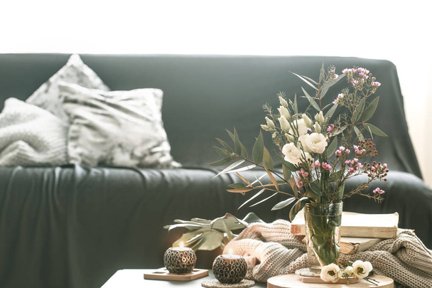gemütliches Wohninterieur mit Dekorelementen im Wohnzimmer mit einem schwarzen Sofa und einer Vase mit Blumen und brennenden Kerzen auf einem kleinen Tisch - Foto, Bild