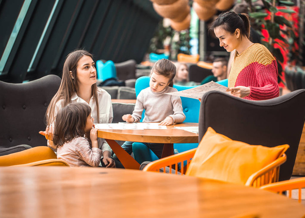 Счастливые молодые женщины с детьми сидят за столом в ресторане. Отдых и общение в ресторане
. - Фото, изображение