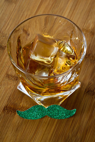 Zblízka na sklenku whisky s knírkem zelené dřevěné pozadí jako koncept pro den svatého Patrika - Fotografie, Obrázek