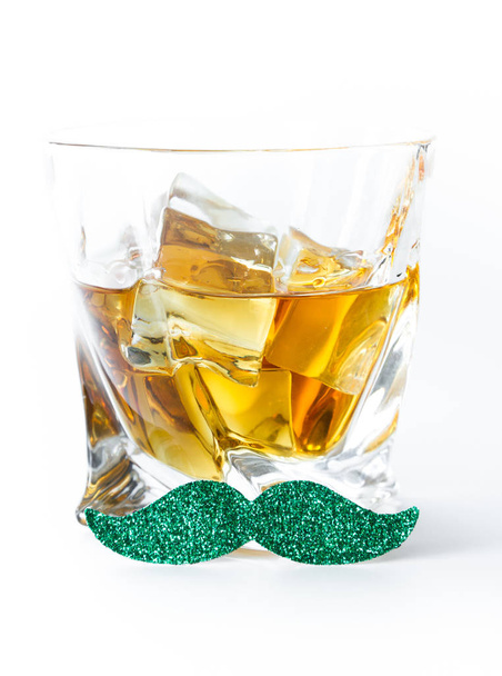 Nahaufnahme eines Whiskeyglases mit grünem Schnurrbart auf weißem Hintergrund als Konzept für den Tag des Heiligen Patricks - Foto, Bild