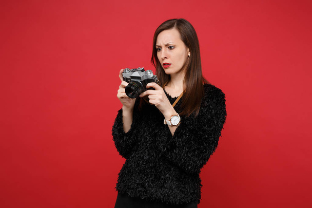Desanimado jovem mulher em camisola de pele preta segurando, olhando para retro câmera de fotos vintage isolado no fundo da parede vermelha brilhante. Pessoas emoções sinceras, conceito de estilo de vida. Mock up espaço de cópia
 - Foto, Imagem