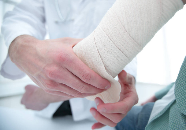 Orthopedist applying bandage onto patients hand in clinic - Photo, Image