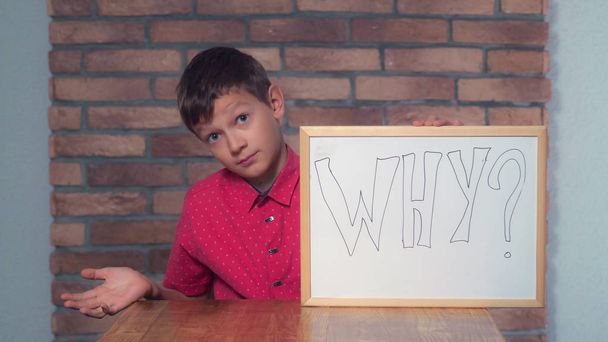 niño sentado en el escritorio sosteniendo el rotafolio con letras por qué o
 - Foto, imagen