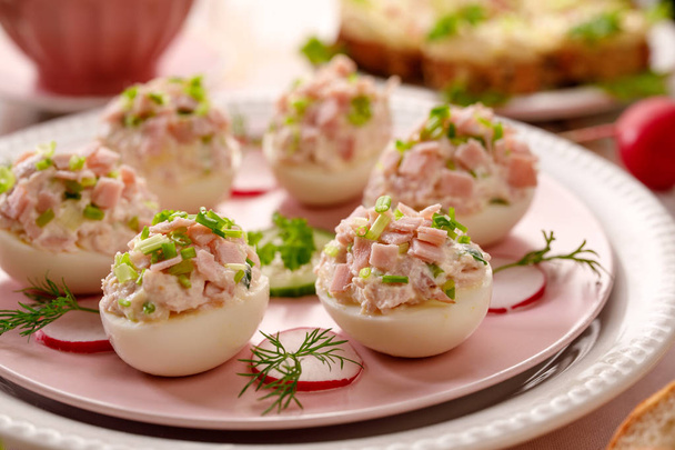 Τα αυγά, Γεμιστά αυγά γεμάτα με μια πάστα που κατασκευάζεται από καπνιστό ζαμπόν, μαγιονέζα, κρόκους αυγών και φρέσκο σχοινόπρασο σε ένα πιάτο. Νόστιμο πρωινό, ορεκτικό για κόμμα ή διακοπών γεύματα - Φωτογραφία, εικόνα