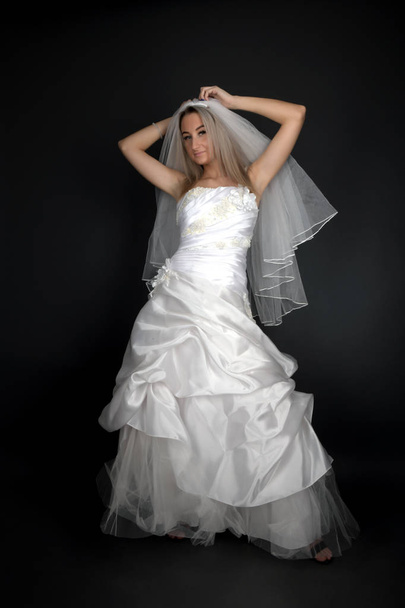 Beautiful blonde bride in a white dress on a black background - Fotó, kép