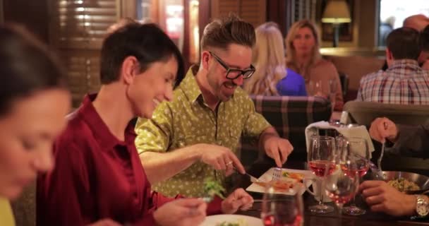 Ein älteres Paar sitzt mit Freunden an einem Tisch in einem Restaurant. Sie genießen Essen und Getränke, während sie miteinander ins Gespräch kommen. - Filmmaterial, Video