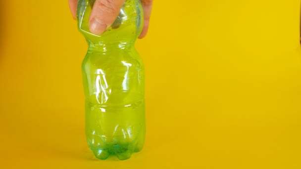 A mans hand crushes a green disposable plastic bottle on a yellow background, footage ideal for topics like ecology and recycling - Footage, Video