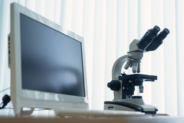Microscope and a personal computer on a table in a laboratory on a window light background. - Valokuva, kuva