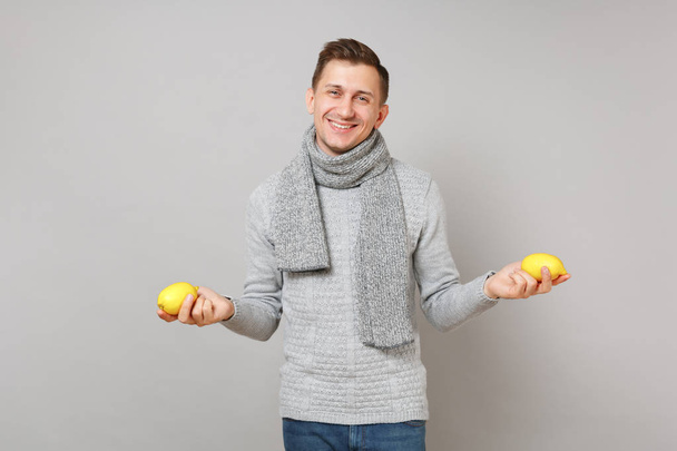 Veselý mladý muž v šedé svetr, šálu drží citrony, samostatný na šedou stěnu pozadí, Studiový portrét. Zdravé módní životní styl, lidé upřímné emoce, chladné období koncept. Vysmívat se kopie prostor - Fotografie, Obrázek