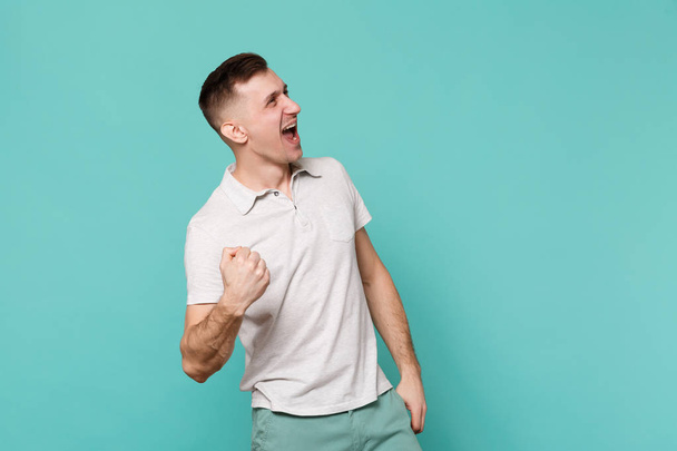 Portrait de jeune homme heureux riant en vêtements décontractés serrant le poing comme gagnant isolé sur fond de mur bleu turquoise en studio. Les gens émotions sincères, concept de style de vie. Maquette espace de copie
 - Photo, image