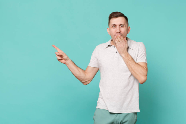Portrait of shocked excited young man in casual clothes covering mouth with palm isolated on blue turquoise wall background in studio. People sincere emotions, lifestyle concept. Mock up copy space - Foto, Bild