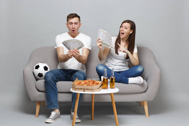 Amazed couple woman man football fans cheer up support favorite team holding fan of money in dollar banknotes, cash money isolated on grey background. People sport family leisure lifestyle concept - Photo, Image