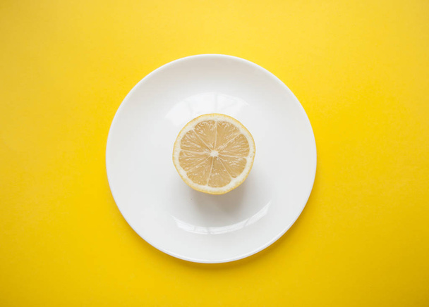 Fresh ripe juicy lemon on white plate on bright yellow background. Minimalistic concept. - Photo, Image