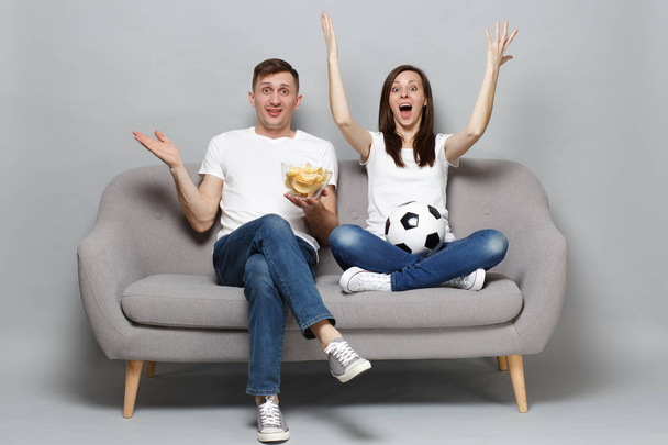 Excited couple woman man football fans cheer up support favorite team with soccer ball, holding bowl of chips sreading rising hands isolated on grey background. Sport family leisure lifestyle concept - Photo, Image