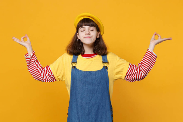 Smiling girl teenager in french beret keeping eyes closed, hold hands in yoga gesture relaxing meditating isolated on yellow background. People sincere emotions, lifestyle concept. Mock up copy space - Photo, Image