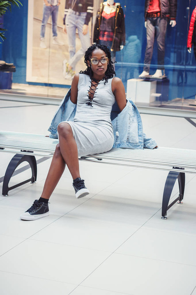 Young dark-skinned woman dressed in casual clothes on the bench in the mall, blurred background - Fotoğraf, Görsel