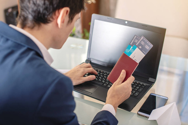 Empresário segurando passagem aérea e passaporte comprando na Internet usando um laptop. Compra e reserva de bilhetes de avião on-line
 - Foto, Imagem