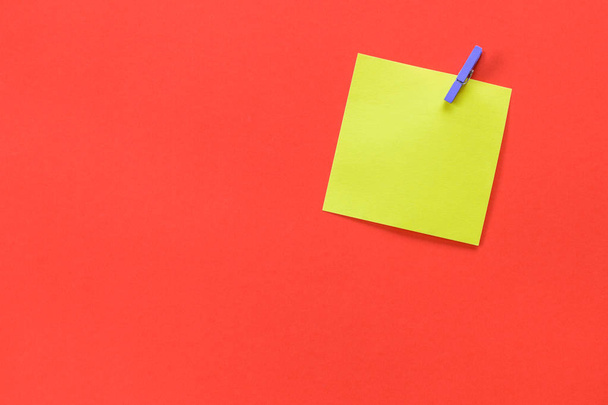 Yellow sticky note attached with a purple peg and copy space isolated on a red /orange background. - Photo, Image