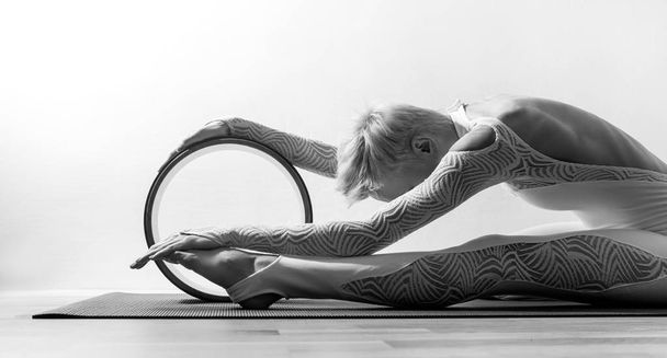 Portrait of gorgeous young woman practicing yoga indoor with a help of yoga wheel. - Foto, Imagen