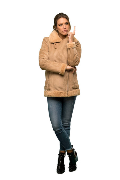 Полнометражный снимок блондинки в пальто, думающей об идее показать пальцем на изолированном белом фоне
 - Фото, изображение