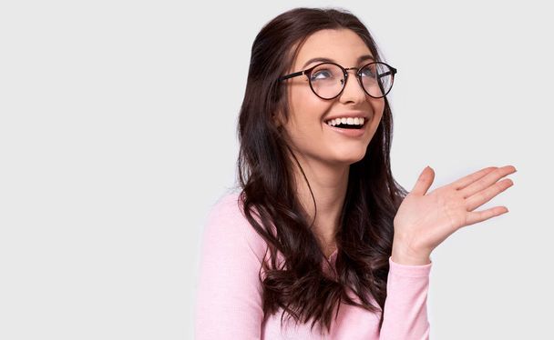 Candid studio portrait of beautiful young woman, broad smile, wears casual outfit and spectacles. Caucasian brunette female in pink blouse posing over white studio wall. People and emotion concept  - Photo, Image