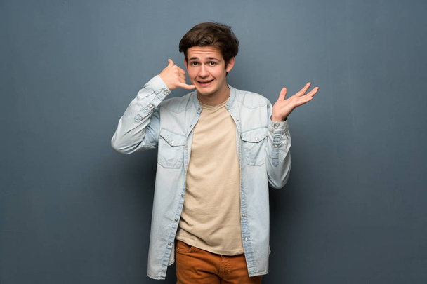 Dospívající muž s jean bundu přes šedou zeď telefon gesto a pochybám - Fotografie, Obrázek