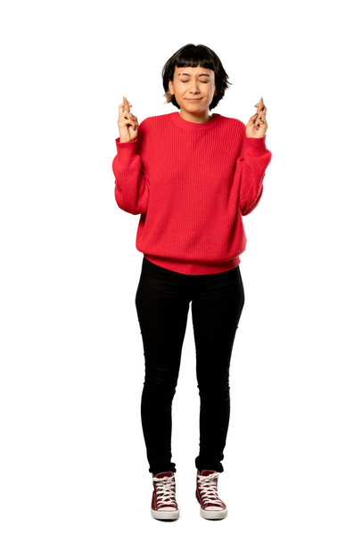 A full-length shot of a Short hair girl with red sweater with fingers crossing and wishing the best over isolated white background - Photo, image